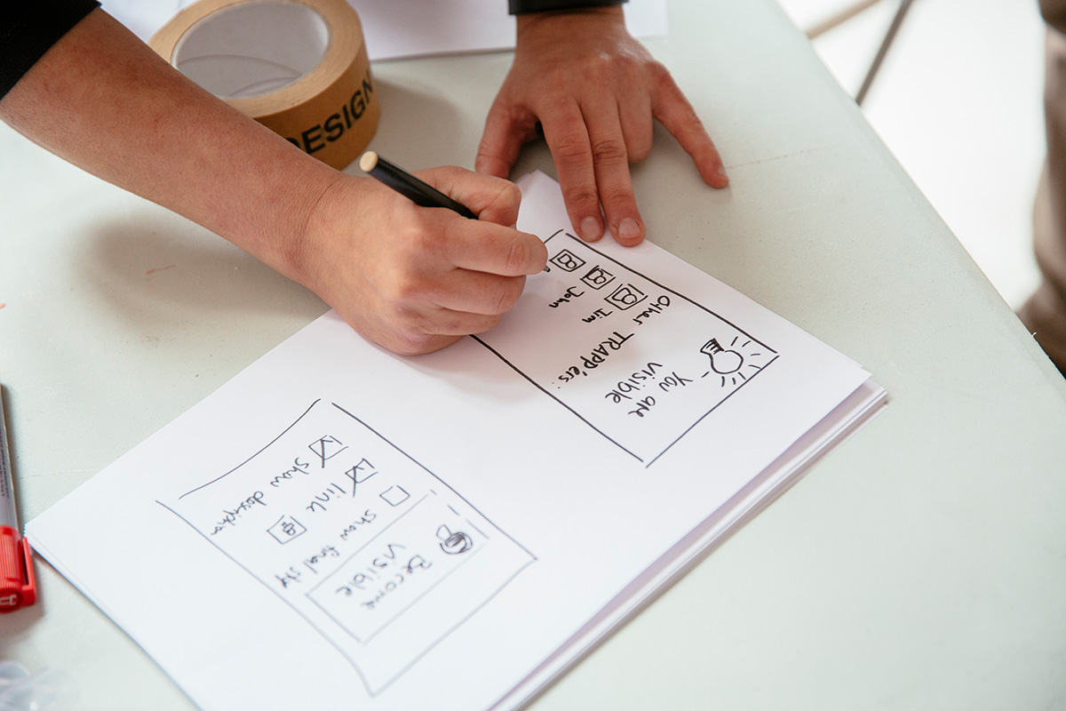 Person drawing a mobile interface on a piece of A4 paper with a Sharpie